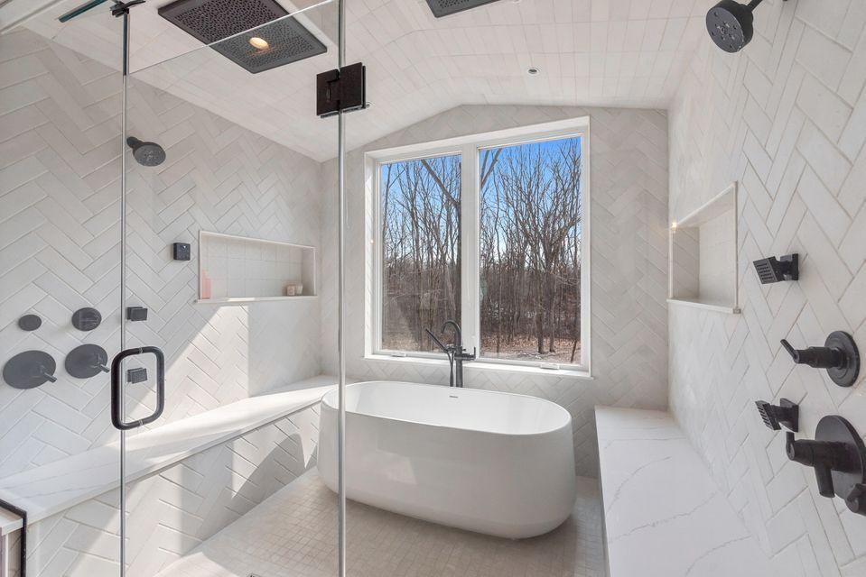 Interior image of bathroom in custom designed home- white tiles, glass shower door and large window.
