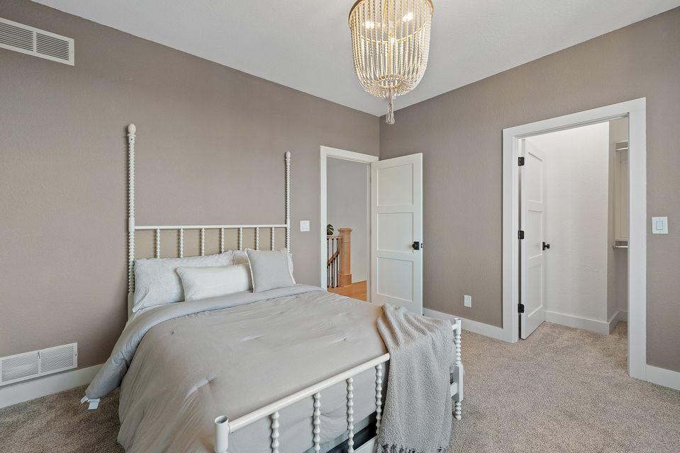 Interior view of bedroom painted taupe with white trim, with carpeted floor and bed.