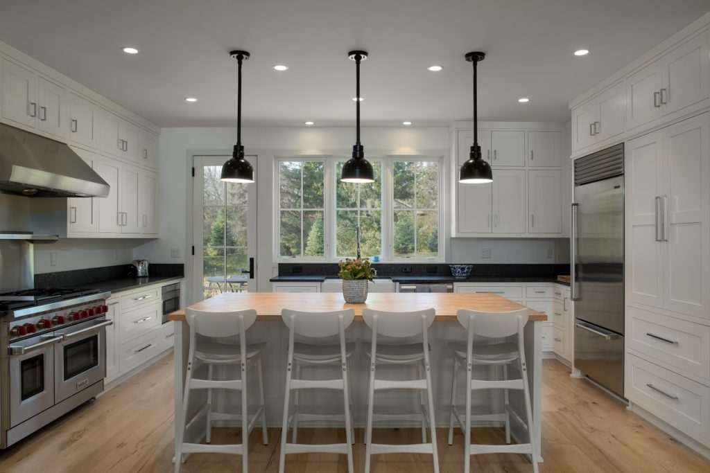 Image of modern kitchen in custom designed home featuring breakfast bar, stools, modern black lighting and appliances.