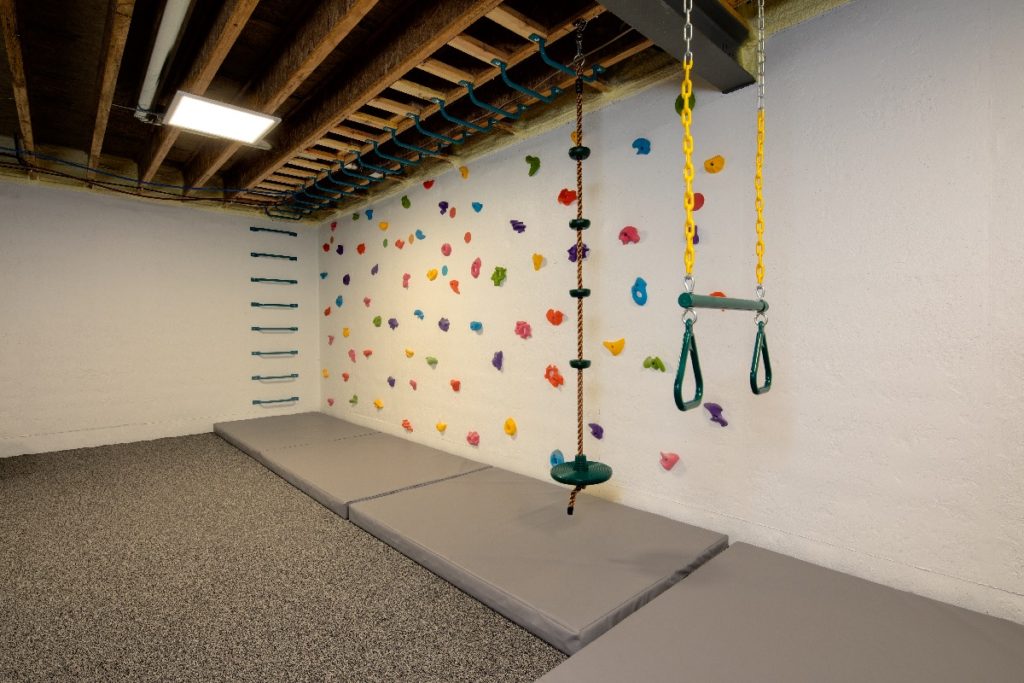 Image of indoor playground in custom built home featuring rock climbing wall, and various swings.
